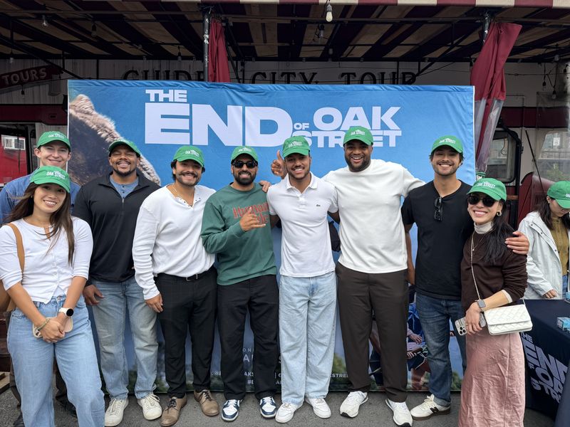 A group of attendees in matching green caps posing together in front of a large printed photo backdrop.